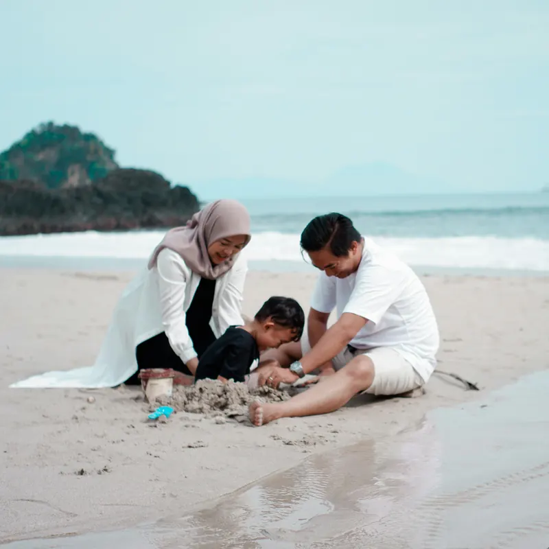A mother in a headscarf, a father and their young son building a sandcastle on a quiet beach