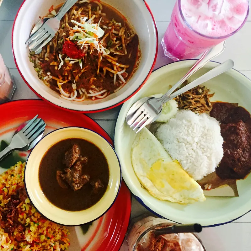 A table of Malaysian dishes: nasi lemak with beef rendang, laksa, curry and rose syrup drinks