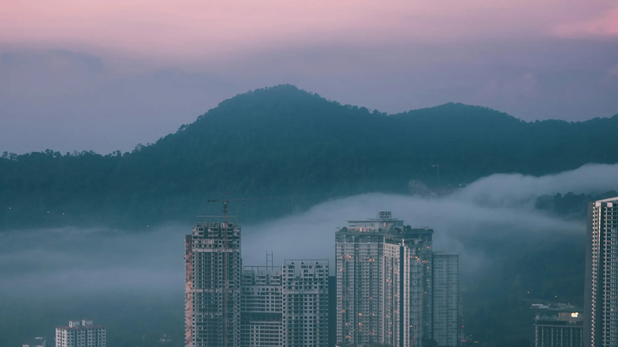 Morning mist drifting between hotels and forested mountains in Genting Highlands