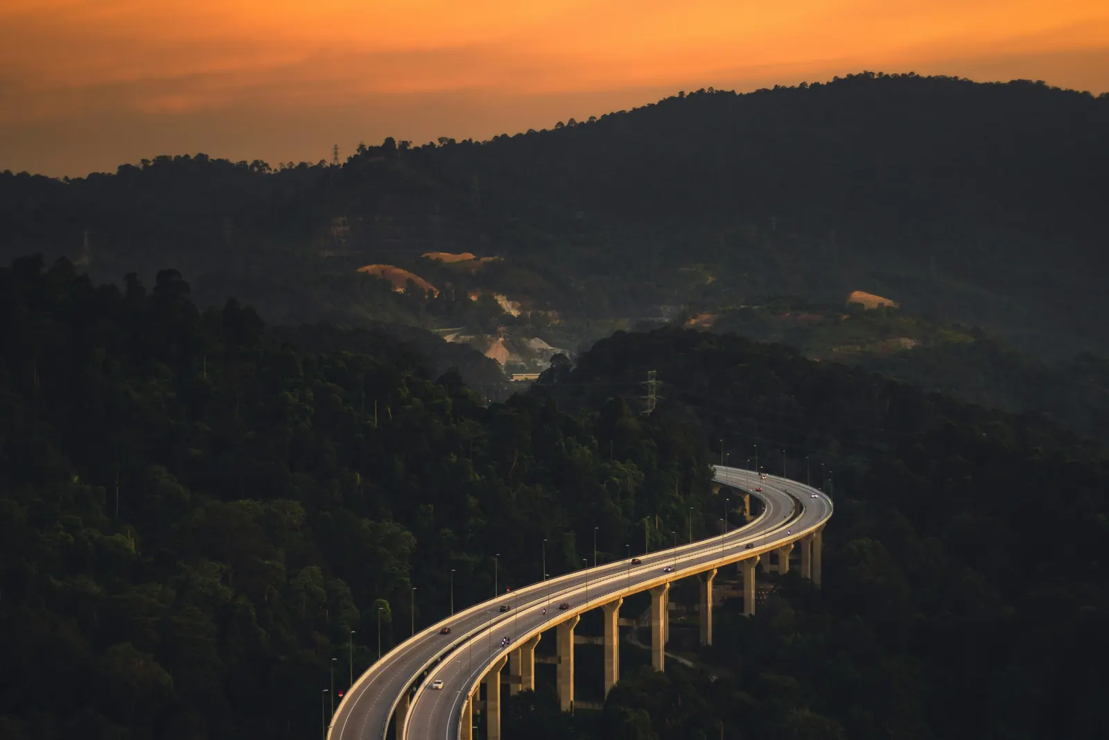 A highway viaduct curving through rainforest hills at sunset on the way to the highlands